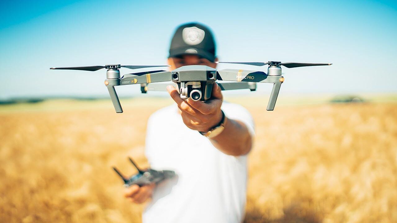 man standing in a field wearing a black hat and holding a remote drone with an attached camera